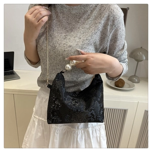 Detail of black snakeskin texture handbag with large pearl handle and gold chain strap