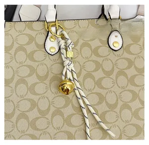 Close-up of stylish woven rope bag charm with golden bell and spring hook detail