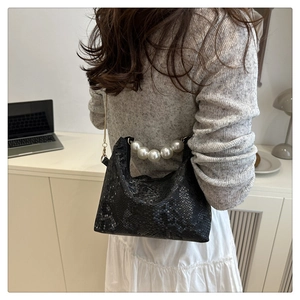 Detail of black snake print bag with elegant pearl handle and gold chain strap