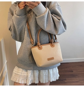 Detail of woven bucket bag showing cream texture, brown leather handle and knotted design