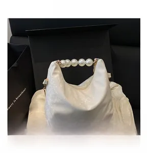 Close-up of white snake-pattern embossed handbag with pearl handle and gold chain strap