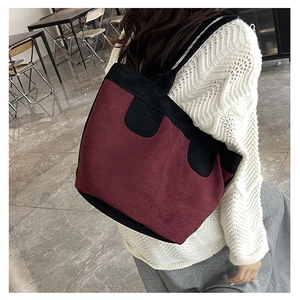 Detail of burgundy and black tote bag in matte suede texture shown on the shoulder