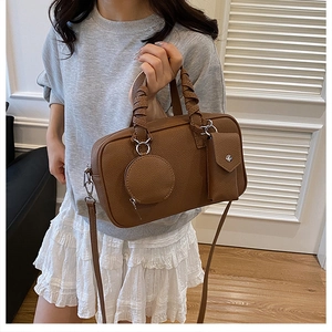 Detail of brown lychee leather Boston bag featuring woven handles and accessory pouches