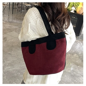 Detail of burgundy faux suede tote bag with black strap accents and matte texture finish