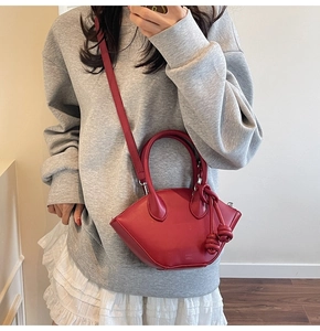 Detail shot of a stylish red shell bag with knot charm worn by a model in casual wear