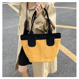 Détail d'un grand sac cabas en daim jaune avec anses noires porté sur un manteau kaki