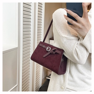 Détail macro de la texture en daim bordeaux et boucle en métal argenté sur le sac