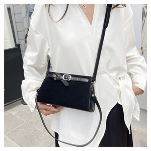 Détail d'un petit sac bandoulière noir mat avec boucle décorative porté sur une chemise blanche