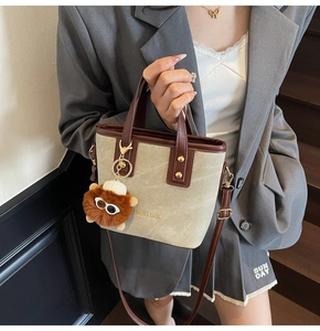 Detail of canvas mini bucket bag featuring brown leather trim and plush ball charm accessory