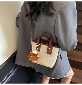 Détail d'un sac seau en toile beige et cuir marron avec un porte-clés lion en peluche