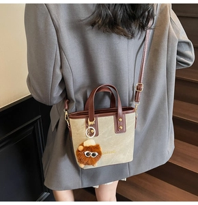 Detail of a beige mini bucket bag with brown leather handles and a plush eye charm