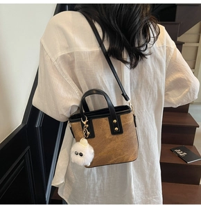 Detail of vintage brown bucket bag with gold rivets and white plush doll charm