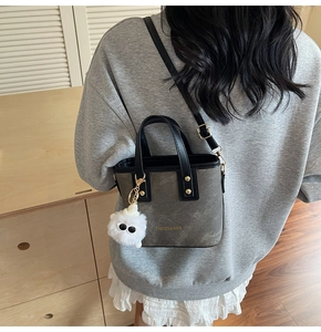 Detail of grey bucket bag with black handles, gold rivets, and a white plush charm
