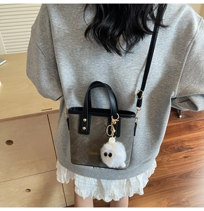 Detail of dark grey bucket bag with matte texture, golden hardware and plush charm