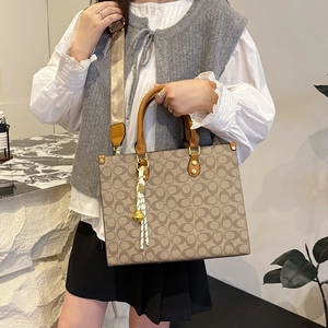 Classic monogram tote bag with brown leather handles and woven tassel charm accessory