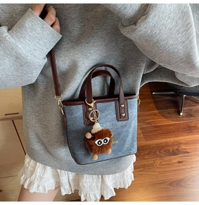Detail of denim tote bag with leather trim and brown plush monster charm on model