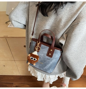 Detail of blue denim tote bag with leather trim and brown plush monster charm on model