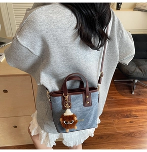Detail of vintage blue denim bucket bag with brown leather trim and plush charm