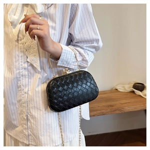 Detail of a black woven evening clutch bag with gold chain strap held by a model