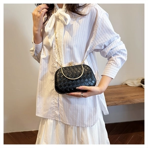 Close-up of black woven handbag with gold arch handle and metal chain strap details