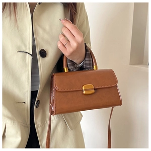 Detalle del bolso de cuero marrón con hebilla dorada combinado con una gabardina beige