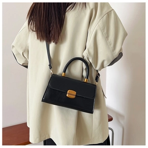 Detalle de bolso vintage de cuero negro con cierre metálico mostrado por una modelo