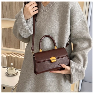 Bolso bandolera vintage de cuero encerado marrón con jersey gris en ambiente acogedor