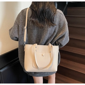 Rear view of a beige pebble leather tote bag shown on a model with a shoulder strap