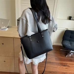 Black pebbled leather tote bag with silver rivets and adjustable strap shown on a model