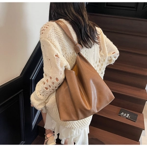 Brown soft leather tote bag with knotted shoulder strap detail on a woman climbing stairs