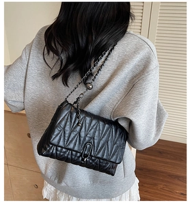 Detail of a black V-quilted leather shoulder bag with a dark metal chain on a model