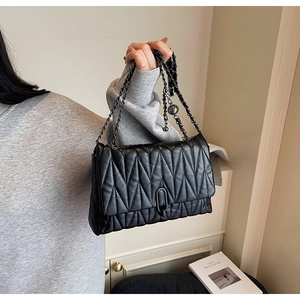 Detail of black quilted chain bag with V-shaped stitching and metallic strap