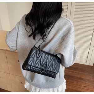 Close-up of black quilted chain bag with elegant metal turn-lock and adjustable ball buckle