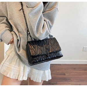 Detail of black quilted crossbody bag with metal chain strap worn by a model