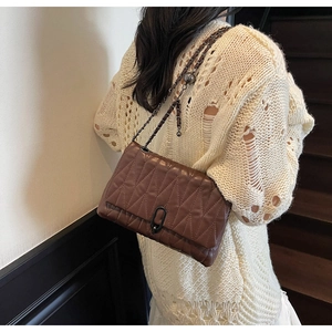 Detail of dark brown quilted crossbody bag with metal chain strap on model's shoulder