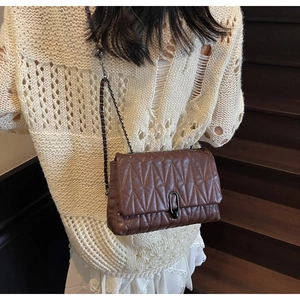 Detail of a dark brown quilted shoulder bag with V-shaped stitching and a metal chain strap