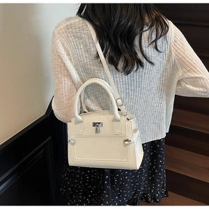 White pebbled leather handbag with silver lock shown on model at a modern staircase