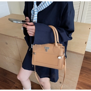Detail of camel lychee grain leather handbag featuring a silver padlock and top handle