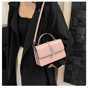 Close-up of a pink crossbody handbag with silver hardware on a black coat outfit