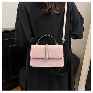 Close-up of a minimalist pink crossbody bag with metal clasp worn over a black coat