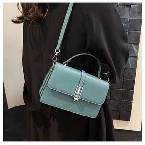Detail of teal leather handbag with metal buckle and slim strap on black outfit