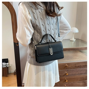 Back view of a woman wearing a black leather crossbody bag with silver buckle detail
