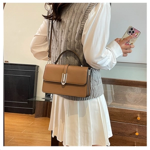 Brown leather crossbody bag shown on model in a cozy interior setting with a shoulder strap