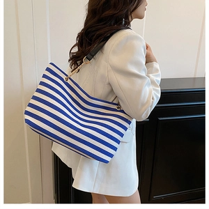 Detail of blue and white striped canvas tote bag with black leather and gold chain strap