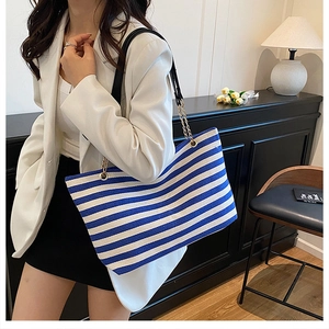 Detail of blue striped canvas tote bag with black leather and gold chain shoulder strap
