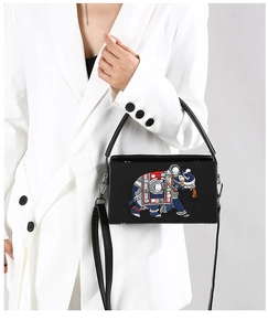 Detailed embroidery of an elephant on a black crossbody bag worn by a model in white