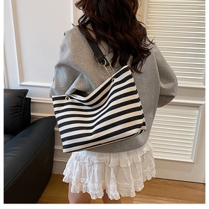 Detail of a large black and white striped tote bag with gold chain strap worn by model