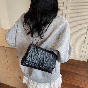 Classic black quilted crossbody bag with metal chain strap worn by a model in a city style