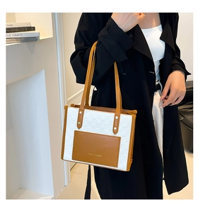 Close-up of a large woven tote bag with brown leather trim worn by a model in a black coat