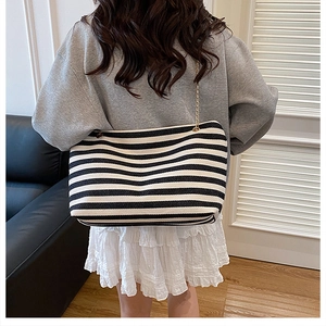 Detail of black and white striped tote bag with gold chain strap on a model shoulder